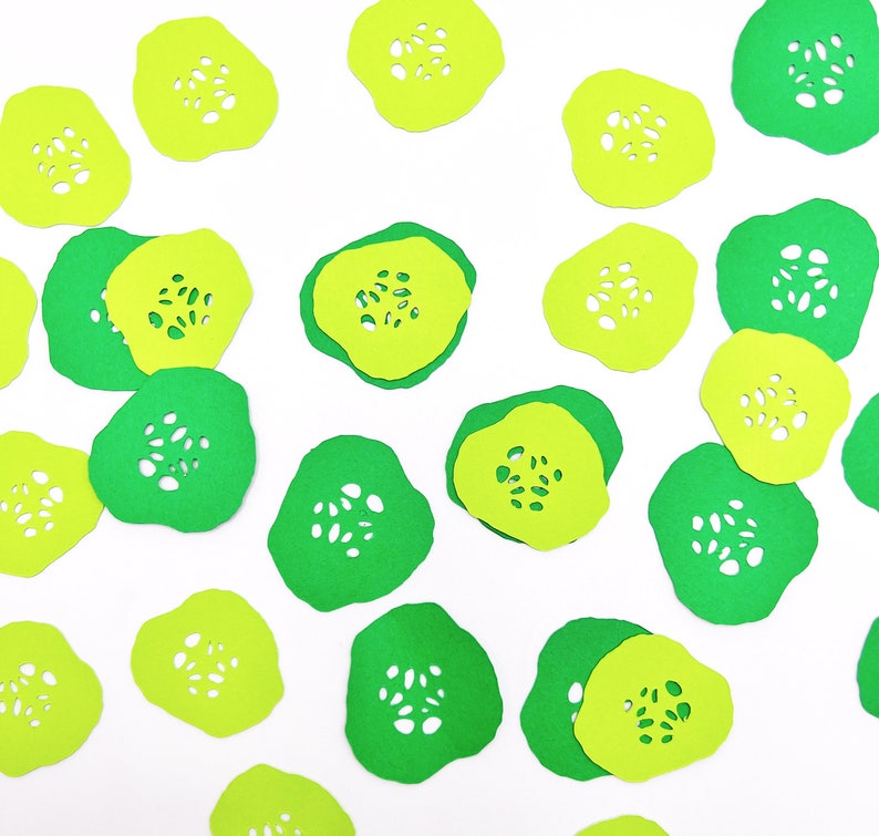 May include: Green and yellow paper cutouts of cucumber slices. The cutouts are scattered on a white background.