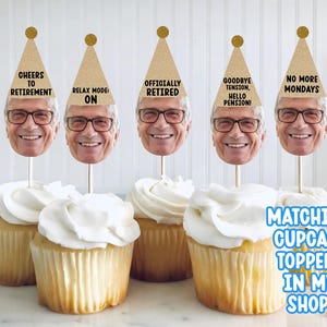 May include: Cupcakes with white frosting and toppers featuring a smiling man's face wearing glasses and a party hat. The hats have phrases like "Cheers to Retirement" and "No More Mondays". The image also includes text that says "Matching Cupcake Toppers In My Shop!"