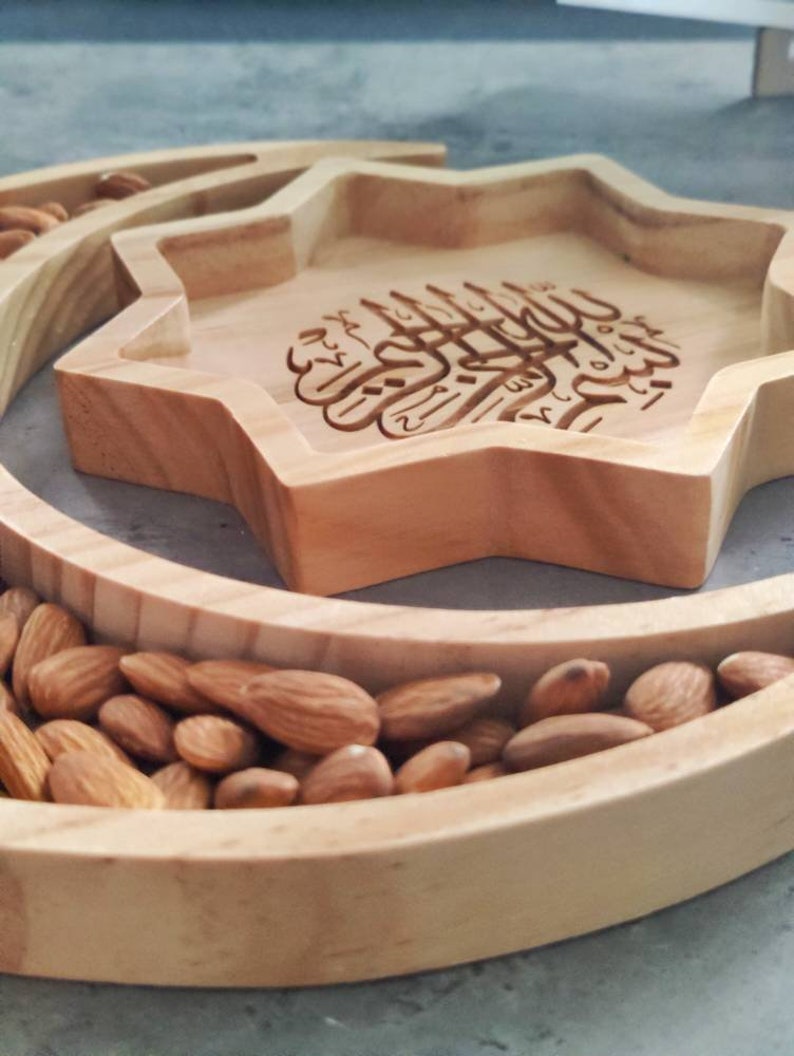 May include: A wooden serving tray with a star-shaped center and a crescent-shaped outer ring. The star-shaped section features engraved Arabic calligraphy. The crescent and star sections are filled with almonds.