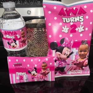 May include: Pink and white party favour bags with Minnie Mouse and a girl's picture. The bags have the text "AYVA TURNS 2" and "TREATS AYVA TURNS 2".