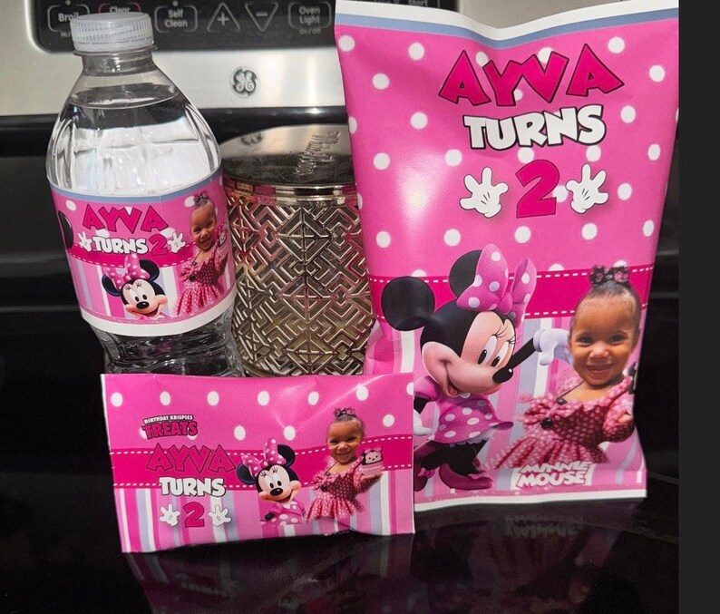 May include: Pink and white party favour bags with Minnie Mouse and a girl's picture. The bags have the text "AYVA TURNS 2" and "TREATS AYVA TURNS 2".