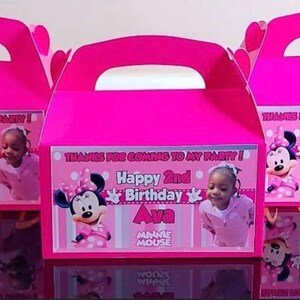 May include: Pink favour boxes featuring Minnie Mouse and a girl's photograph. The boxes are decorated with the text "Thanks for coming to my party! Happy 2nd Birthday Ava Minnie Mouse".