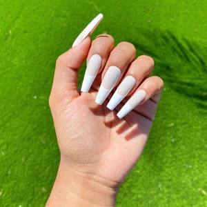 May include: A hand with long, white, almond-shaped fake nails with a white tip and a nude base.