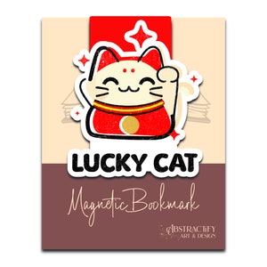 May include: A red and white lucky cat bookmark with a gold coin on its chest. The bookmark is magnetic and has the text "LUCKY CAT" and "Magnetic Bookmark" on it. The text "ABSTRACTIFY ART & DESIGN" is also on the bookmark.