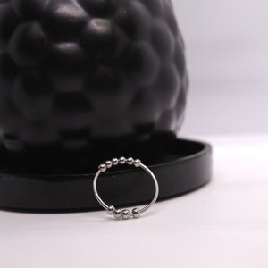 May include: A silver ring with a series of small, round beads. The ring is on a black surface.