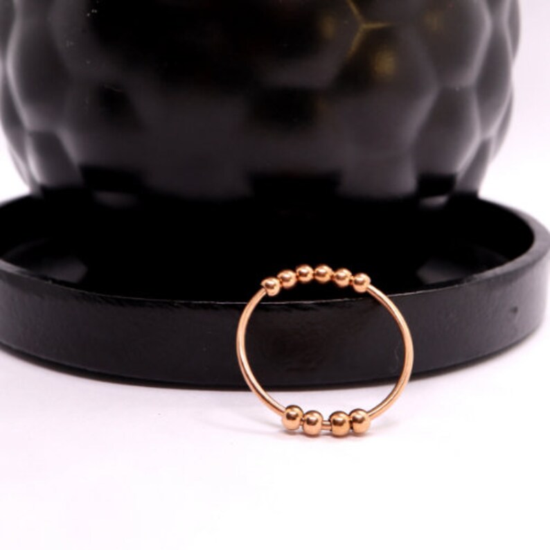 May include: A rose gold ring with a row of small, round beads.