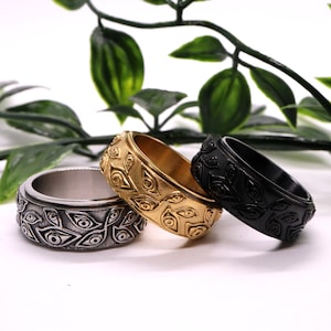 Op de afbeelding: Drie ringen van roestvrij staal met een herhalend oogontwerp. De ringen zijn in goud, zilver en zwart.