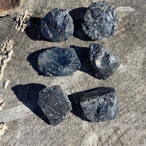 May include: Six black obsidian stones of various shapes and sizes. The stones are rough and have a natural, unpolished finish.