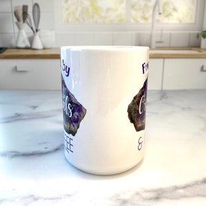 Peut inclure: Une tasse en c&eacute;ramique blanche avec un motif de cristal d'am&eacute;thyste violet et le texte "Fueled by Crystals & Coffee".