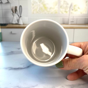 Peut inclure: Une tasse en c&eacute;ramique blanche avec une anse. La tasse est vide et a une finition lisse et brillante.
