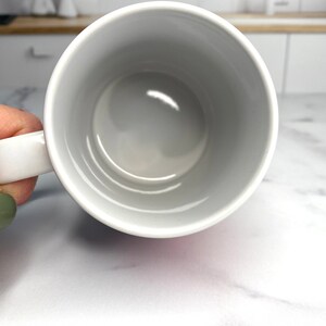 May include: White ceramic mug with a smooth, glossy finish. The mug is empty and has a rounded handle.