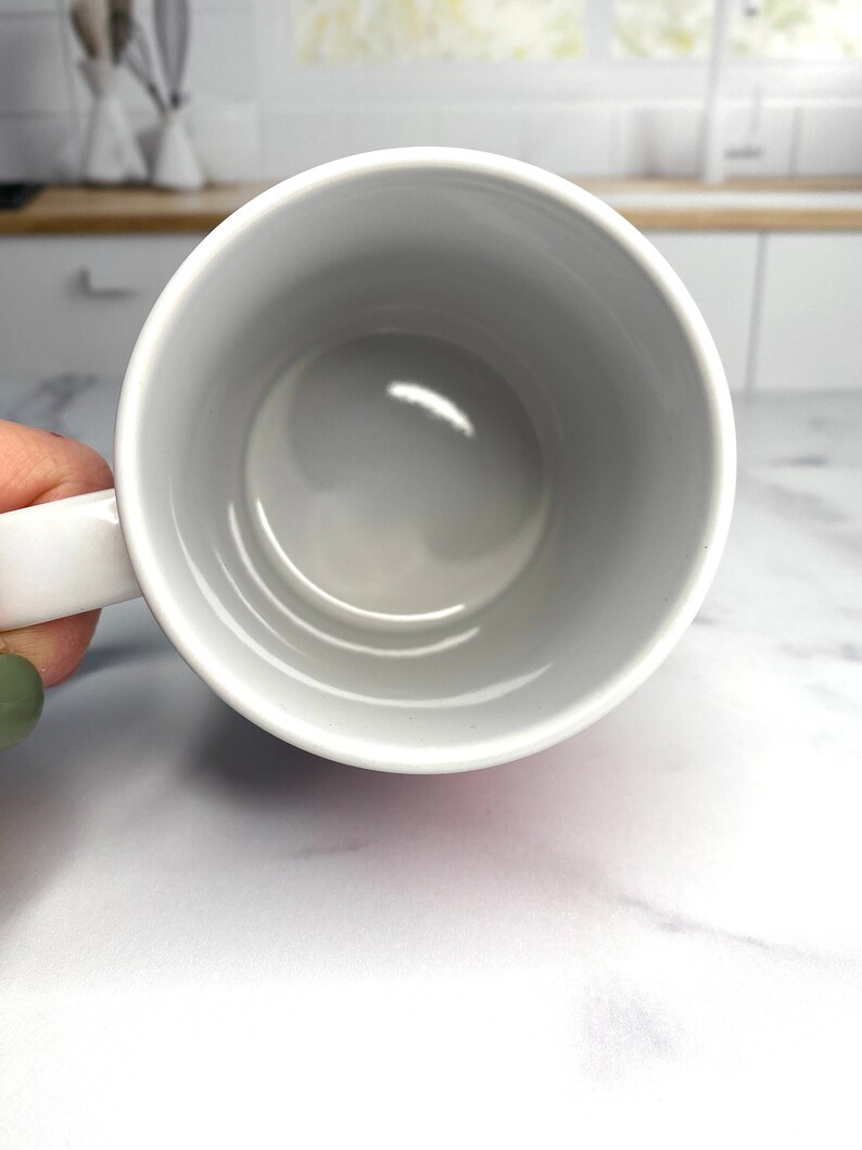 May include: White ceramic mug with a smooth, glossy finish. The mug is empty and has a rounded handle.