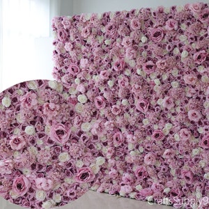 Pode incluir: Uma grande parede floral feita de flores artificiais rosa e brancas. A parede é composta por muitas flores pequenas, criando um visual cheio e exuberante.