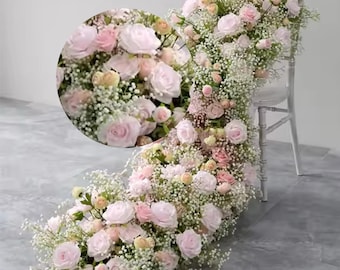 Puede incluir: Una larga guirnalda de rosas rosas y aliento de bebé blanco drapeada sobre una silla blanca. La guirnalda es perfecta para una boda u otro evento especial.