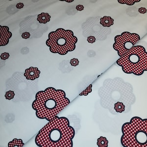 Könnte beinhalten: Weißer Stoff mit einem sich wiederholenden Blumenmuster. Die Blumen sind rot-weiß kariert mit marineblauen Umrissen. Das Design umfasst unterschiedlich große Blumen. Der Stoff ist gefaltet und zeigt die Kontinuität des Musters.