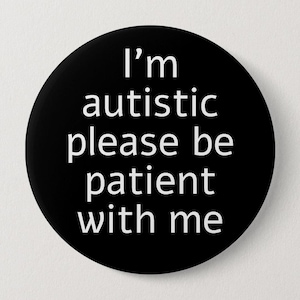 May include: A circular black pin-back button featuring white sans-serif text that reads, I'm autistic please be patient with me. The design is centered on the round surface, providing a clear and legible message against the solid black background.