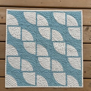 以下が含まれることがあります： 青と白のキルトで、半円形の幾何学模様が施されています。キルトは渦巻き模様でキルティングされています。