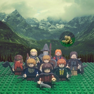 May include: A group of nine Lego minifigures from the Lord of the Rings movie franchise. The figures are standing on a green Lego baseplate in front of a mountainous landscape. The figures include Gandalf, Aragorn, Legolas, Gimli, Frodo, Sam, Merry, Pippin, and Gollum.