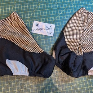 May include: Pair of black and tan shoe covers with a mesh upper and elasticized openings. The covers have a black base with a light gray accent and are designed to fit over shoes. A small card with the text "AuntMoSews" is in the background.