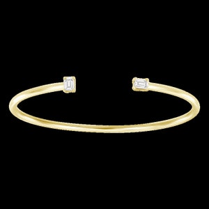 May include: A gold bangle bracelet with two small, rectangular, clear gemstones.