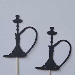 May include: Two black silhouette cupcake toppers shaped like hookahs with a long stem and a round base. The toppers are attached to wooden sticks.