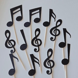 May include: A set of black glitter musical note and treble clef cupcake toppers. The toppers are on wooden skewers.