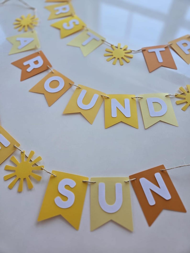 Puede incluir: Una pancarta de papel amarilla y naranja con las palabras "First Trip Around The Sun" y recortes de sol.