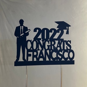 May include: Black silhouette cake topper with a graduation cap, the year 2022, the word "Congrats", and the name "Francisco".