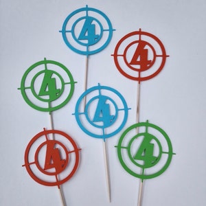 May include: Six cupcake toppers featuring a target with the number "4" in the center. The targets are in blue, green, and orange.