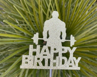 May include: Gold glitter cake topper featuring a silhouette of a person lifting weights with the text "Happy Birthday".