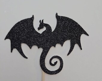 May include: Black glitter dragon cake topper with a curled tail. The dragon is on a wooden stick.