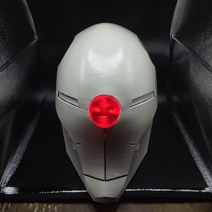 May include: A white helmet with a red light in the center. The helmet has a sleek, futuristic design.