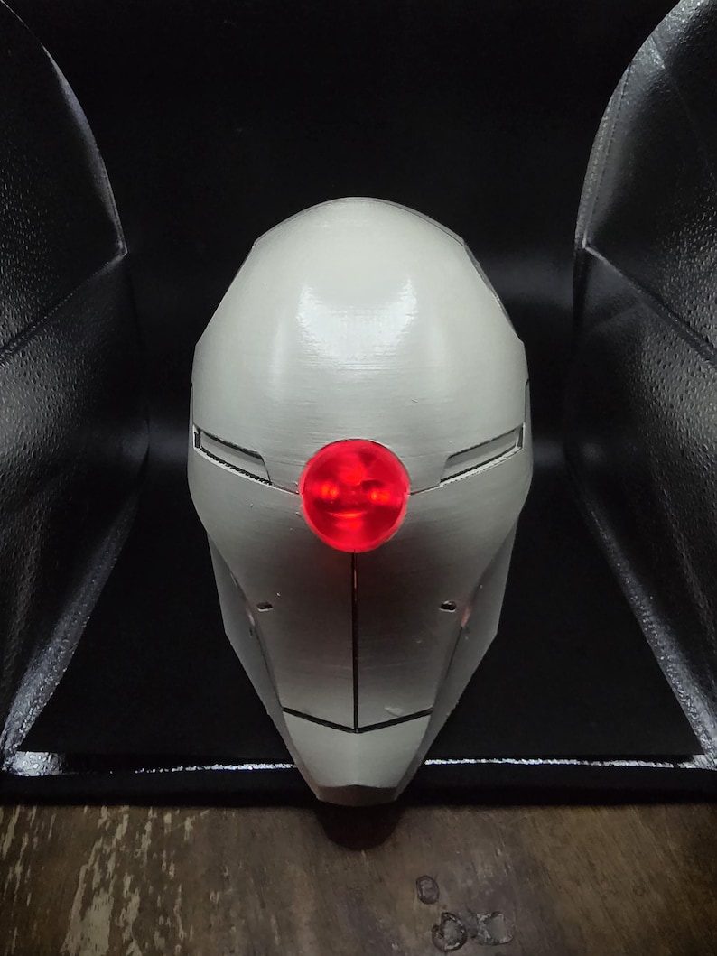 May include: A white helmet with a red light in the center. The helmet has a sleek, futuristic design.