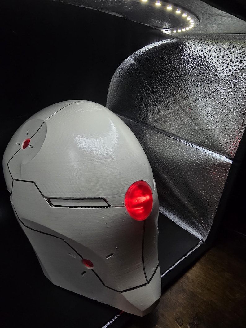 May include: A white helmet with black lines and red lights. The helmet is made of a smooth, hard material and has a rounded shape.