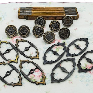 May include: An assortment of antique hardware components, including ornate metal buckles and decorative buttons. A wooden folding ruler is also present. The items are arranged on a floral patterned fabric.