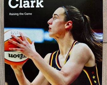 May include: A magazine cover featuring Caitlin Clark, with the title "Caitlin Clark" in large white letters against a black background. The text "Raising the Game" is below the name. Clark is holding a basketball, wearing a navy and yellow jersey.