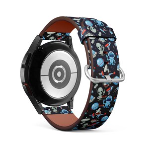 Peut inclure: Une montre connectée noire avec un bracelet en cuir marron orné d'un motif répété d'extraterrestres bleus, de vaisseaux spatiaux et d'étoiles rouges sur un fond bleu foncé.