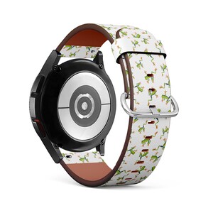 Puede incluir: Una correa de reloj blanca con un patrón de ranas verdes. La correa está hecha de cuero y tiene un forro de cuero marrón. La correa de reloj está diseñada para un Samsung Galaxy Watch.