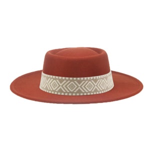 Könnte beinhalten: Ein rostfarbener Filzhut im Fedora-Stil mit breiter Krempe und einem weißen und beigefarbenen Band mit geometrischem Muster um die Krone.