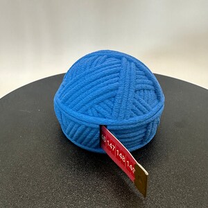 Könnte beinhalten: Eine blaue Garnkugel mit einem roten Maßband, das herausragt. Die Garnkugel liegt auf einer schwarzen Oberfläche.