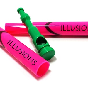 May include: Two pink markers with the word "ILLUSIONS" printed on them. One marker is lying on its side, and the other is standing upright. There is a green plastic object with a hole in the middle.