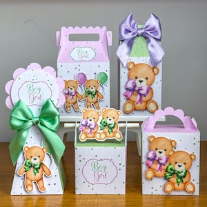 Pode incluir: Cinco caixas de presente brancas com bordas recortadas e alças, decoradas com bolinhas verdes e roxas e ilustrações de ursinhos de pelúcia marrons. Cada caixa apresenta o texto Boy or Girl e é acentuada com grandes laços de cetim verdes ou roxos.