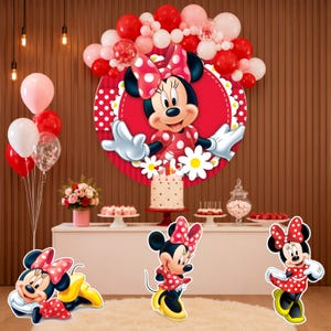 May include: A party decoration set featuring a large circular backdrop with a Minnie Mouse illustration, red and white polka dot patterns, and white daisies. Includes three separate Minnie Mouse cutouts and a balloon arch in red, pink, and white.