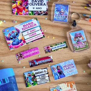 Può includere: Una collezione di etichette rettangolari personalizzate e due portachiavi in plastica trasparente con vari personaggi dei cartoni animati tra cui Roblox, Sonic, Stitch, Mario, Barbie, Spider-Man, Minecraft, Frozen e Winnie the Pooh con nomi.