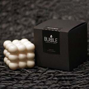 May include: A white soy wax candle in the shape of a cube with rounded edges. The candle is made by Bubble Handmade Soy Candles and is labeled "Walk to Relax".