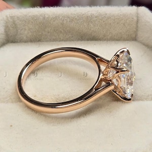 May include: Rose gold engagement ring with a large, clear, marquise-cut diamond. The ring is presented on a light grey velvet surface. The band is smooth and polished, with a delicate design supporting the diamond.