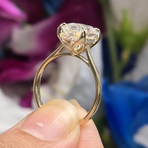 Könnte beinhalten: Ein goldener Verlobungsring mit einem großen, klaren, runden Diamanten, der in einer zarten Krappenfassung sitzt. Der Ring hat ein schlichtes Band.