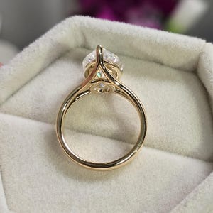 May include: A gold engagement ring with a large, round, clear diamond set in a prong setting. The ring is in a white velvet ring box.