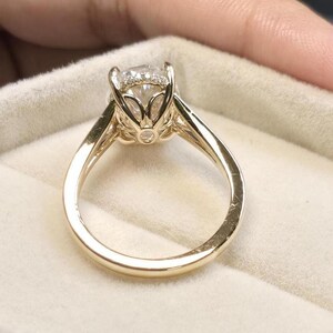 May include: A gold engagement ring with a large, round, clear diamond set in a delicate, floral-inspired setting. The ring is displayed in a white velvet ring box.