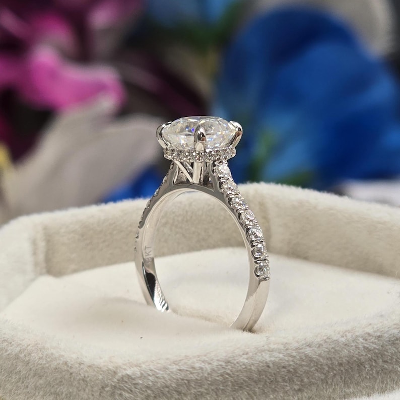 May include: A sparkling engagement ring with a large, round-cut diamond as the centerpiece. The ring features a delicate band adorned with smaller diamonds, creating a halo effect around the main stone. The ring is set in a white metal, likely platinum or white gold.